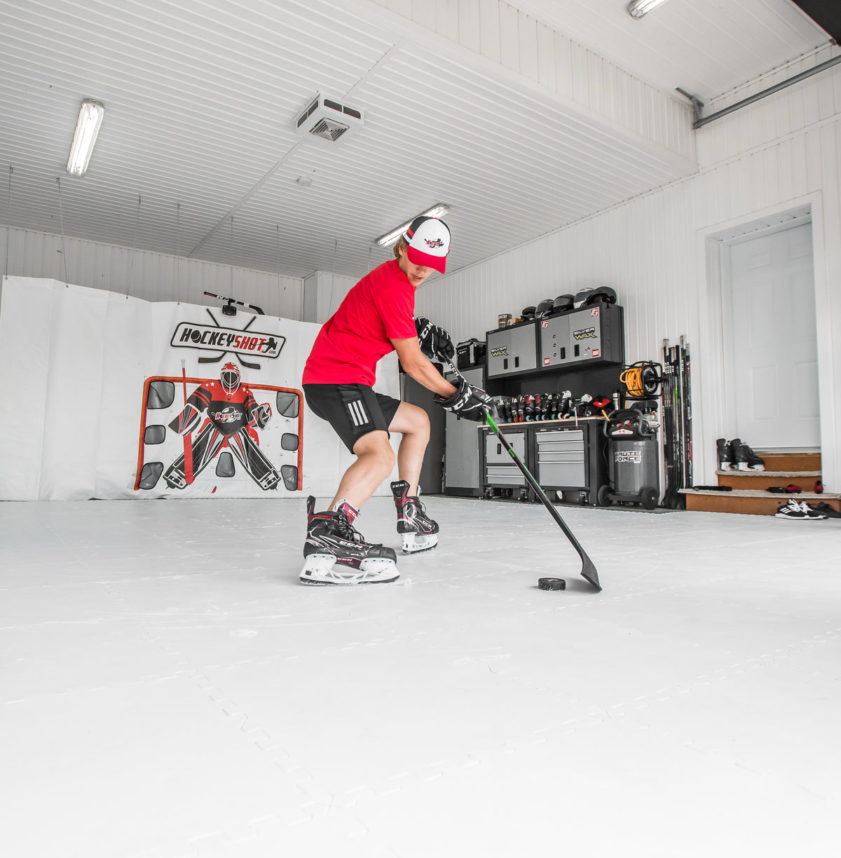 Hockey player shooting a puck on synthetic ice tiles in a home garage training rink, with a HockeyShot shooting target in the background.